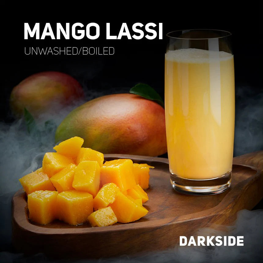 Glass of mango lassi next to fresh mango slices on wooden board with whole mangoes in background